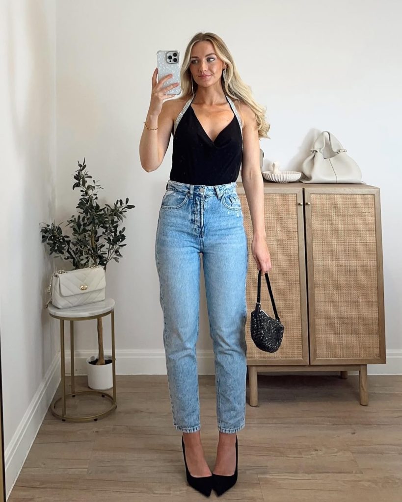 A woman wearing a black velvet halter top with silver straps and light-wash denim jeans.
