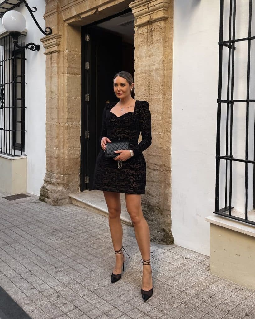 A woman in a black lace mini dress with long sleeves and strappy high heels.