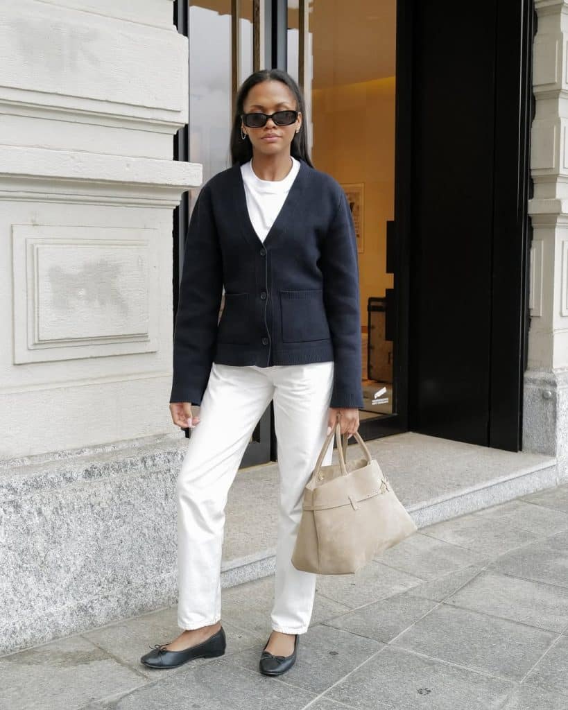 A woman in a navy cardigan and white trousers standing on a city street.