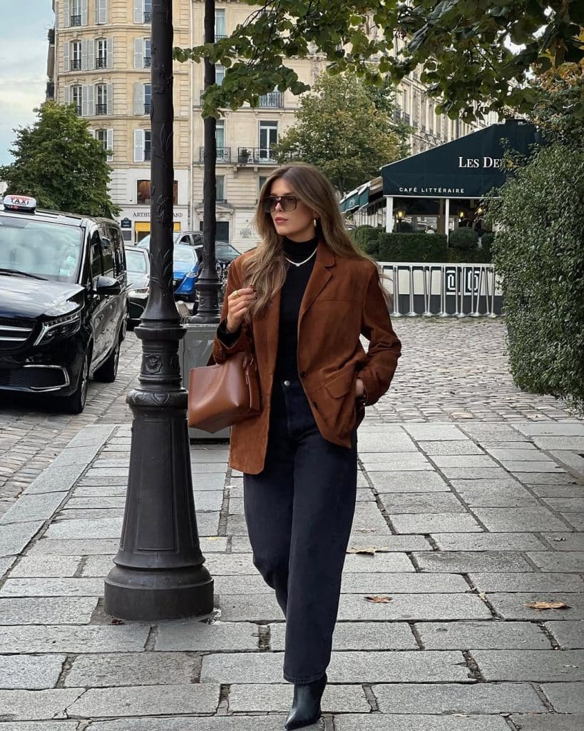 Woman in a brown suede blazer and wide-leg jeans walking on a cobblestone street.