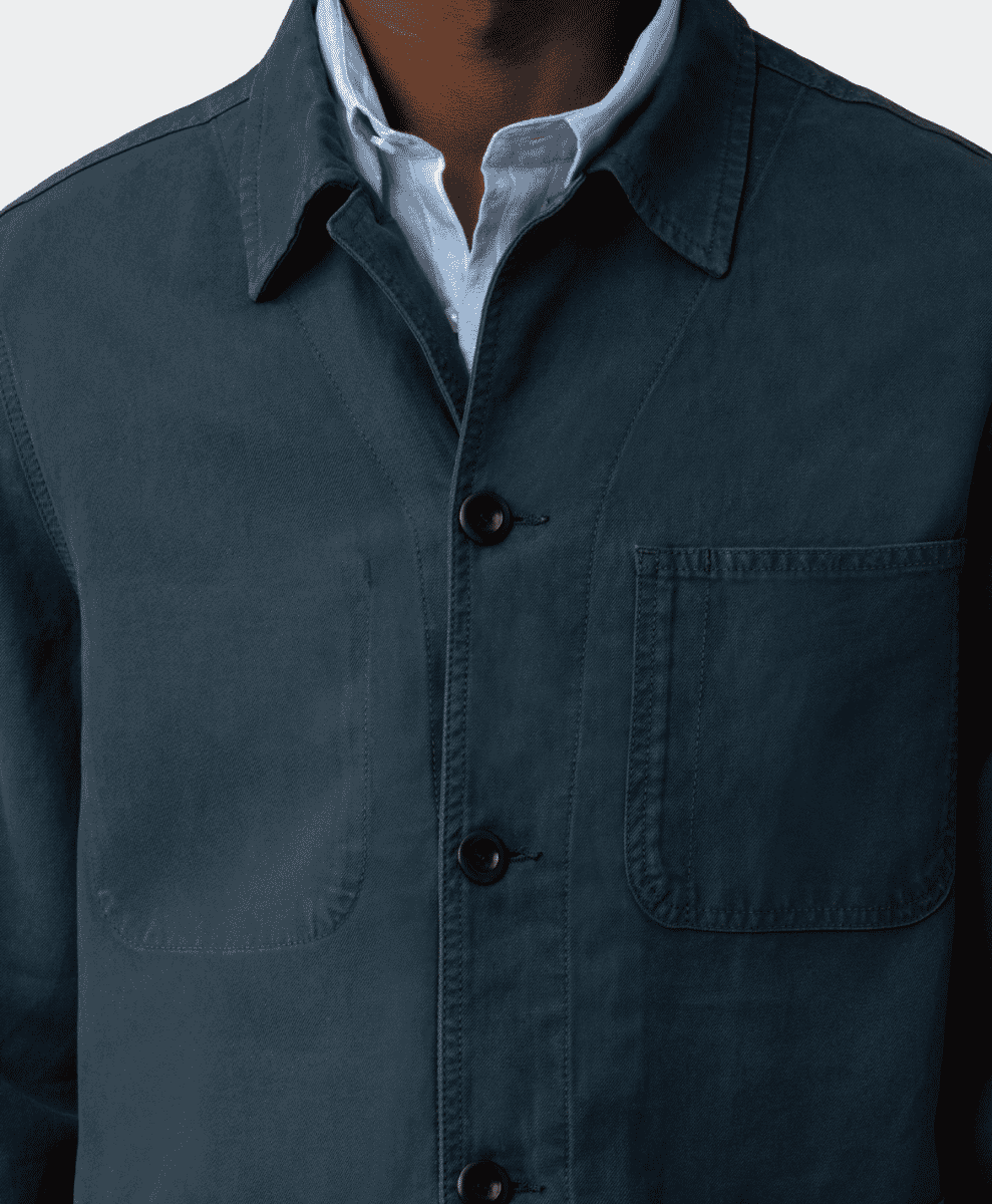 Close-up of a man wearing a dark teal utility jacket over a light blue collared shirt.