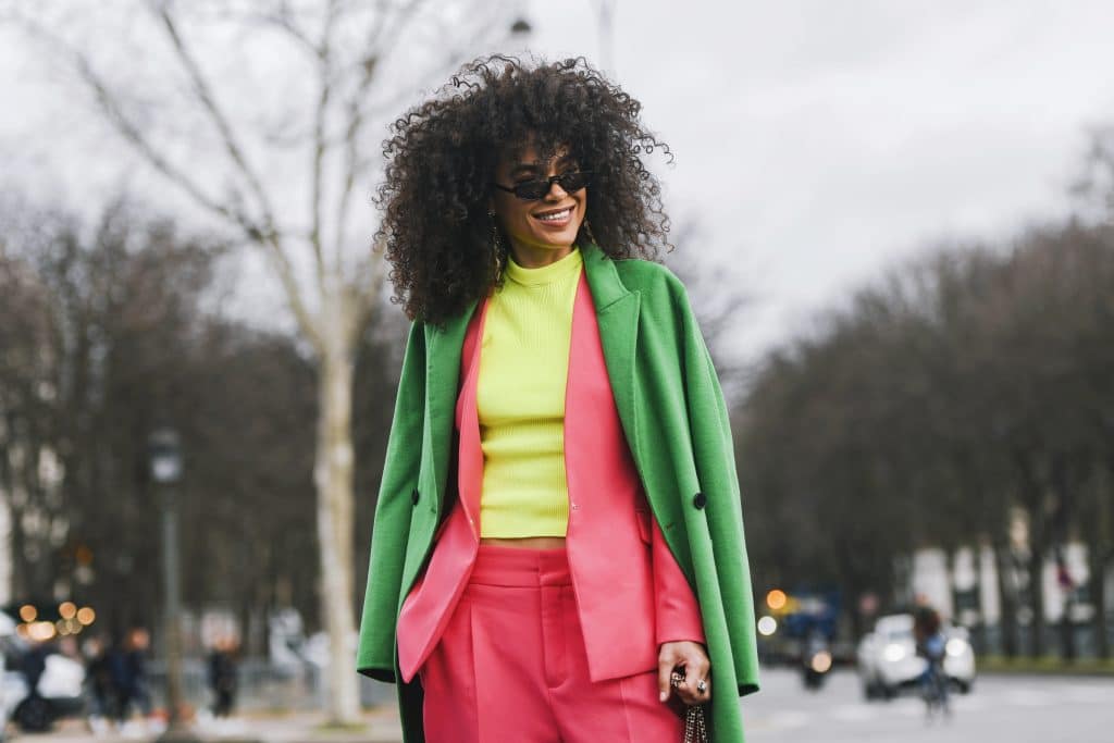 A woman with curly hair wearing a neon green coat and pink suit in an urban environment.