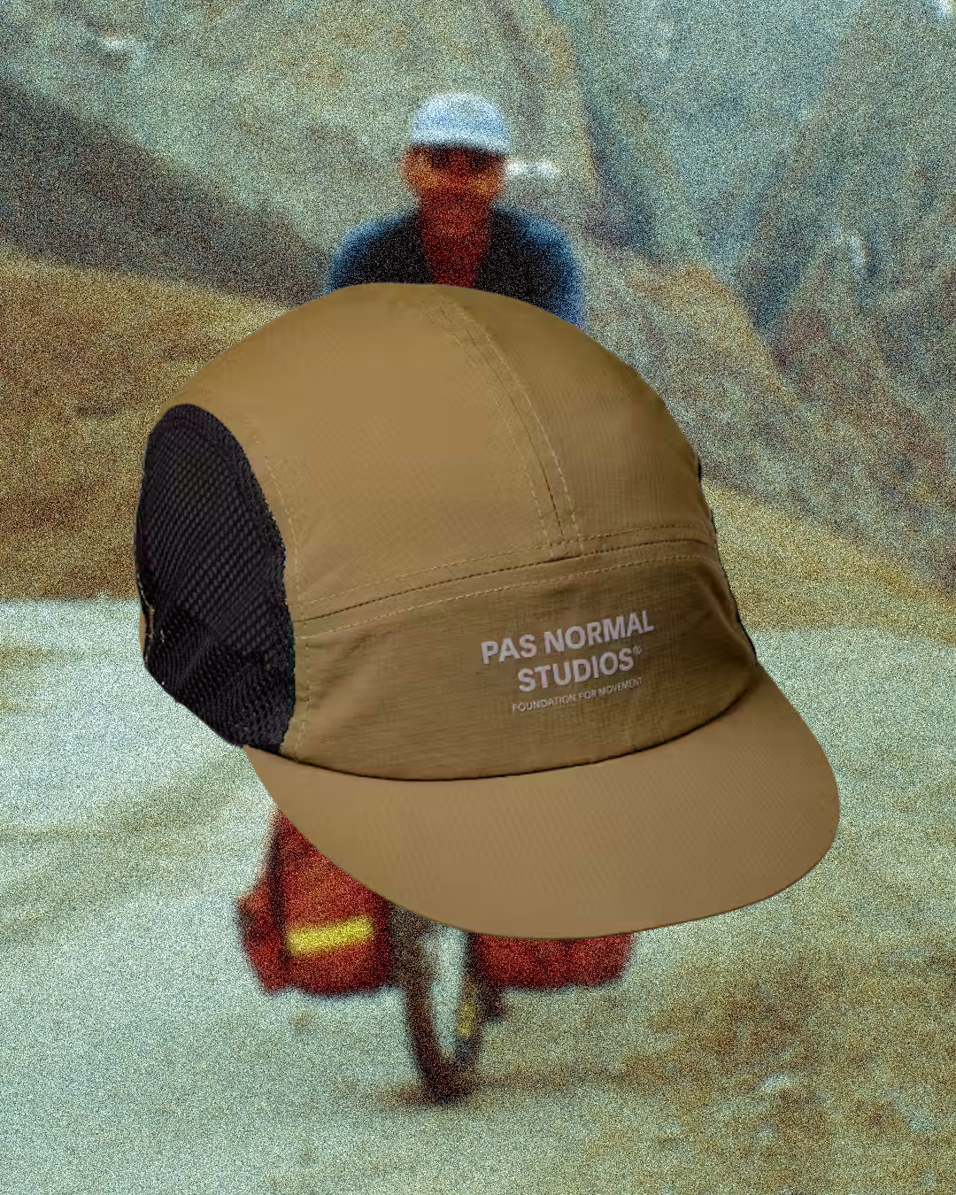 Cyclist riding a gravel path with a mud-flecked face and the cap brim tilted down to block facial debris.