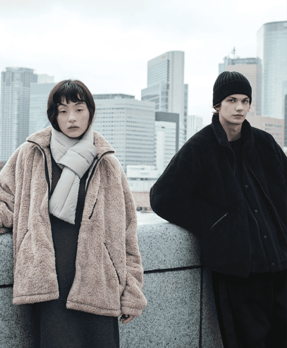 Models in beige fleece and a white puffer scarf against a city skyline.