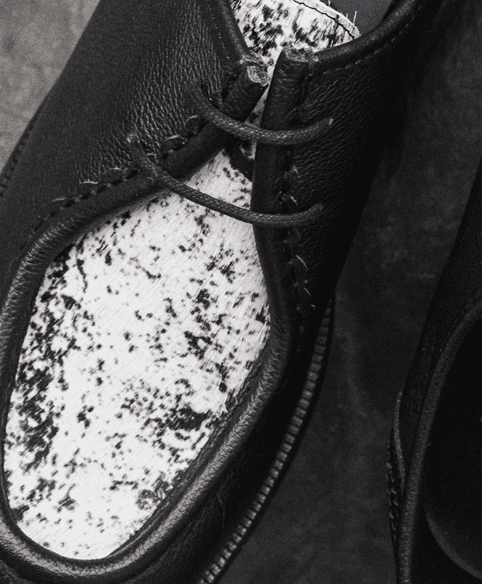 Monochrome detail shot of a leather shoe's stitching, laces, and textured insole.