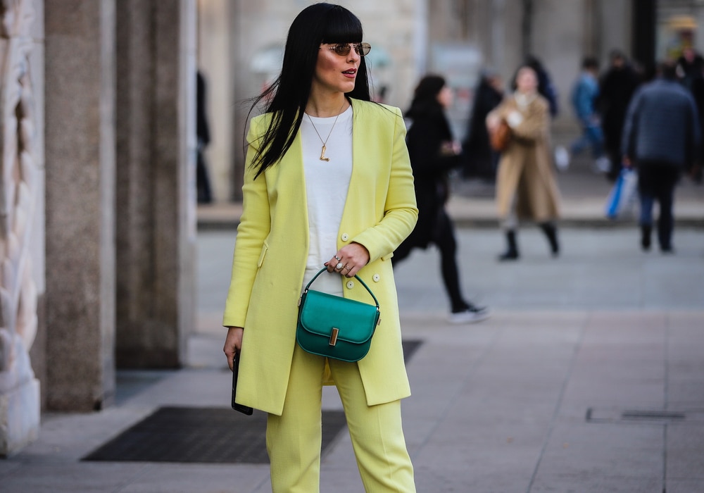 A woman walking in a city street wearing a vibrant monochrome yellow suit and matching overcoat.