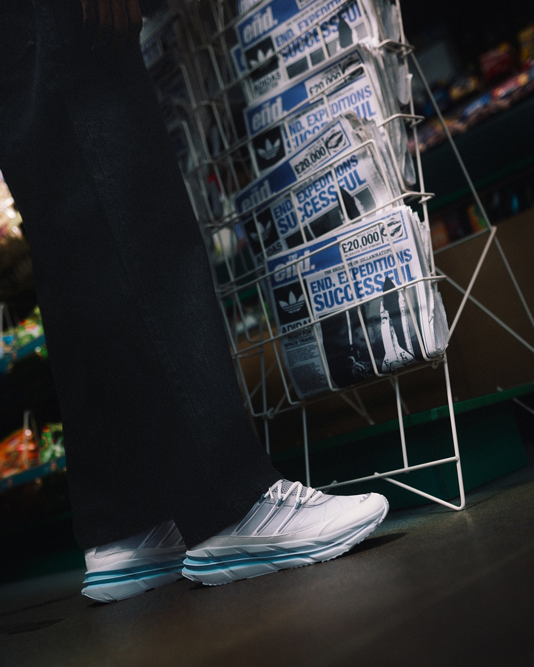 A person wearing the adidas sneakers with black pants standing next to a newspaper rack.