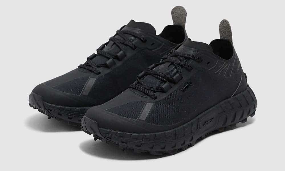 A pair of all-black Norda trail running shoes emphasizing the rugged Vibram Megagrip Litebase sole.