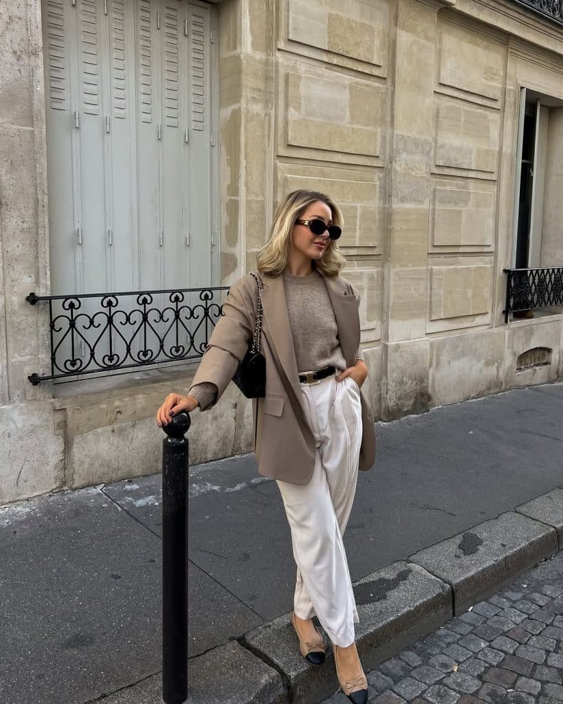 A blonde woman in a beige blazer and white wide-leg trousers on a Parisian street.
