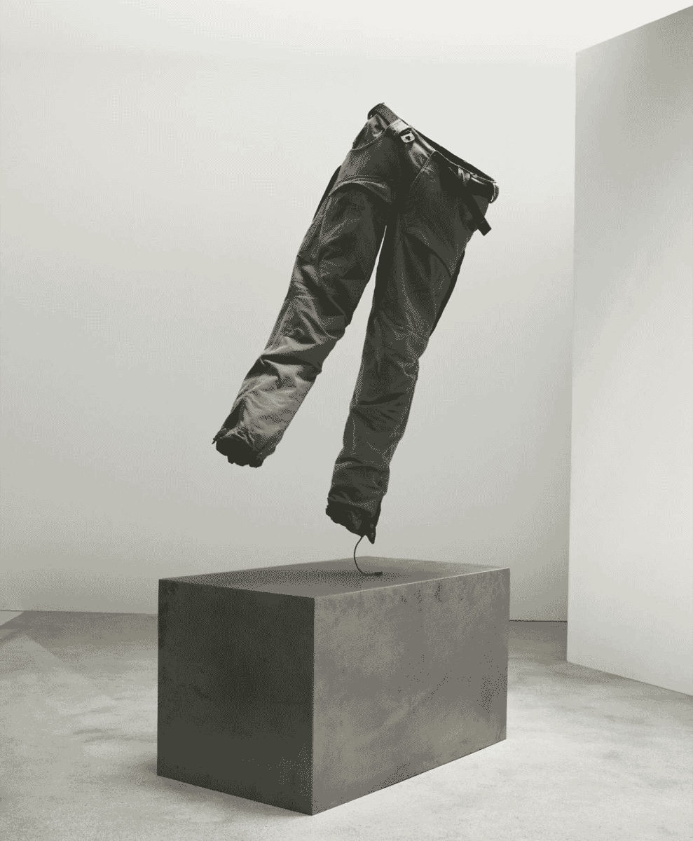 Dark rugged outdoor trousers floating above a concrete block in a minimalist space.