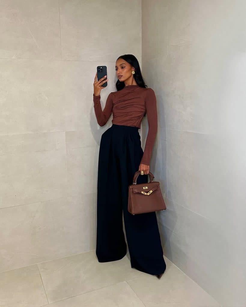Mirror selfie of a woman wearing a ruched brown long-sleeve top and high-waisted black wide-leg trousers.