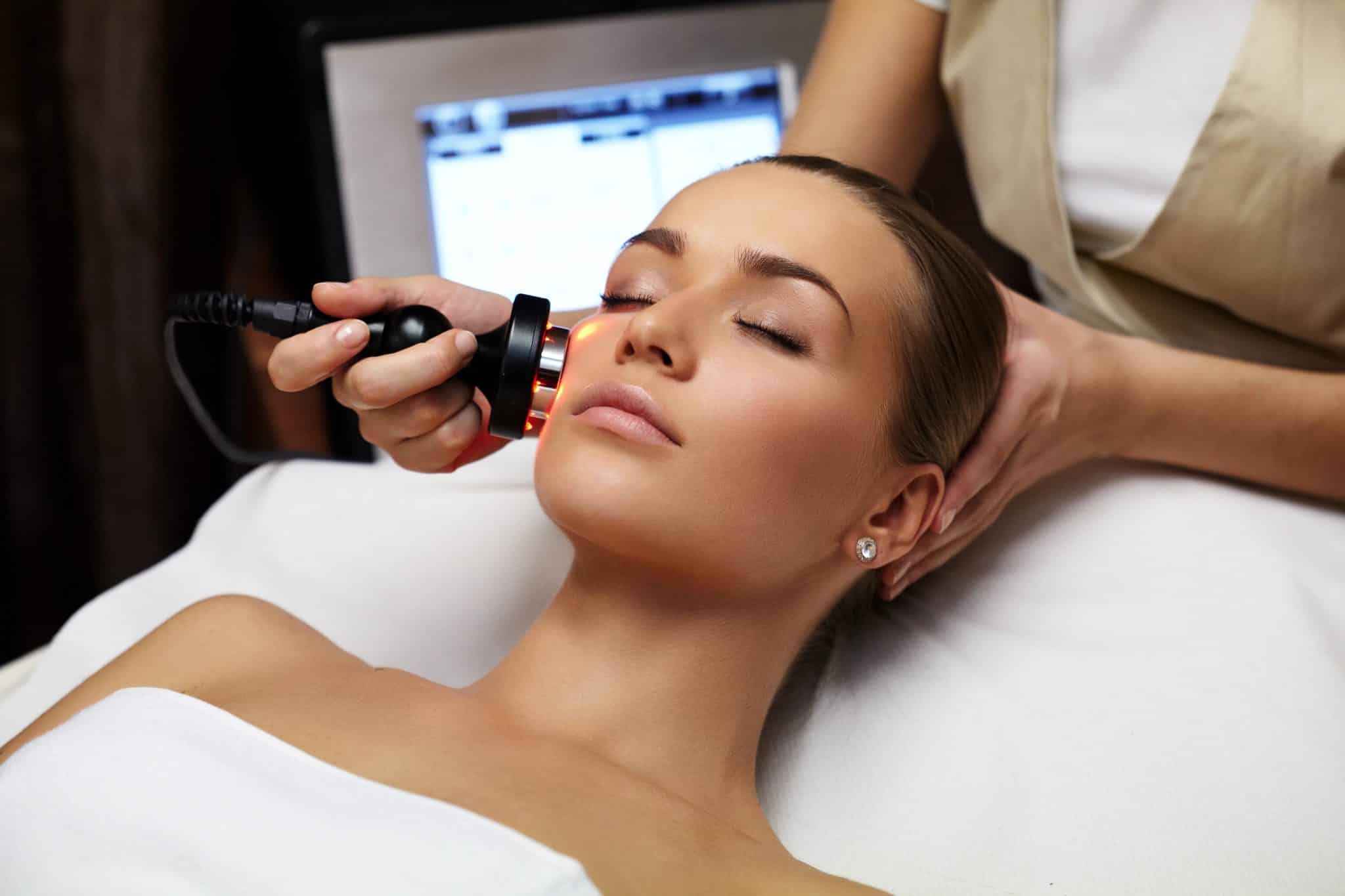 A woman receiving a facial treatment with a red light therapy device in a luxury wellness environment.