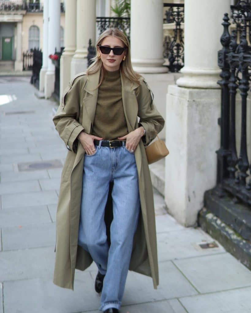 Woman in an olive trench coat and olive turtleneck walking down a city street.