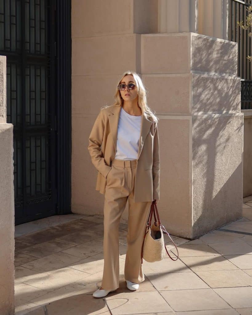 A woman in a light camel suit paired with a simple white t-shirt and woven tote bag.