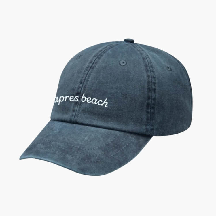 A white baseball cap with 'Apres Beach' embroidered in green font.