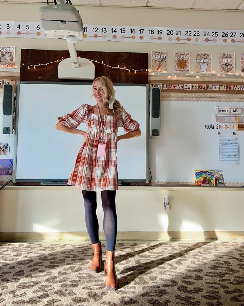 A teacher in a red and white plaid dress with puff sleeves in a classroom.