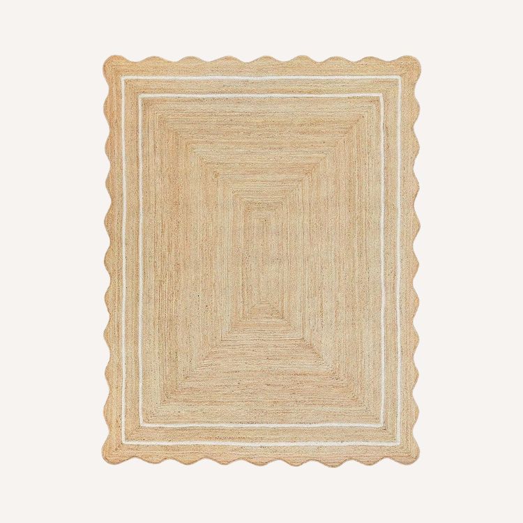 Natural jute rug with a scalloped edge on a wooden floor.