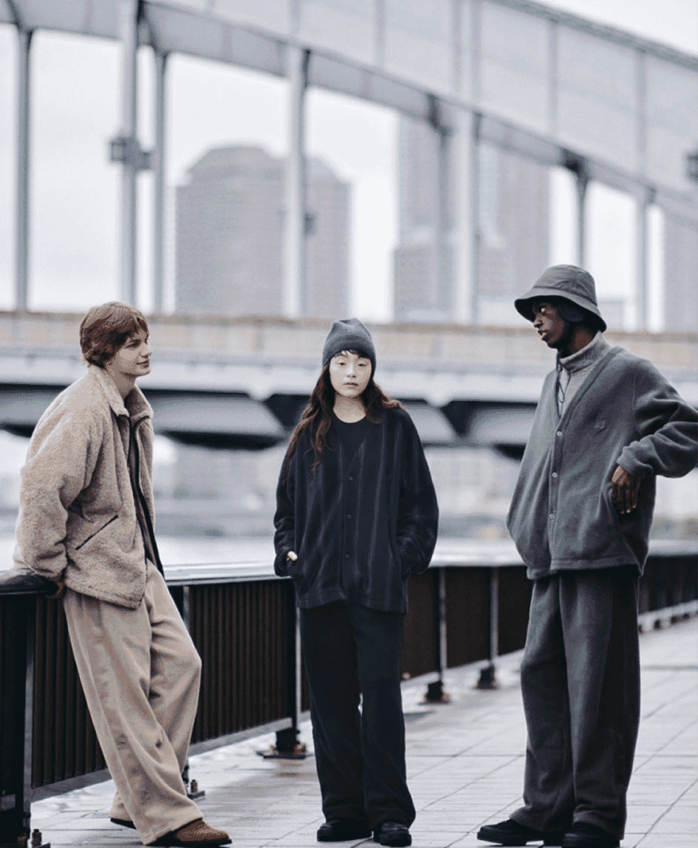 Models in wide-leg pants and fleece jackets standing under a city overpass.