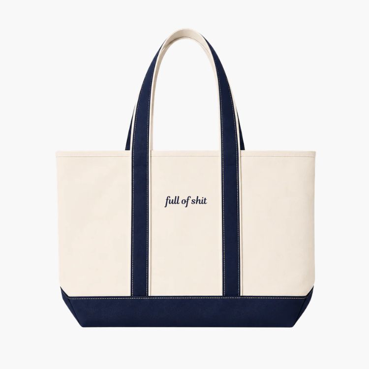 A white canvas boat tote with navy trim and 'full of shit' embroidery.