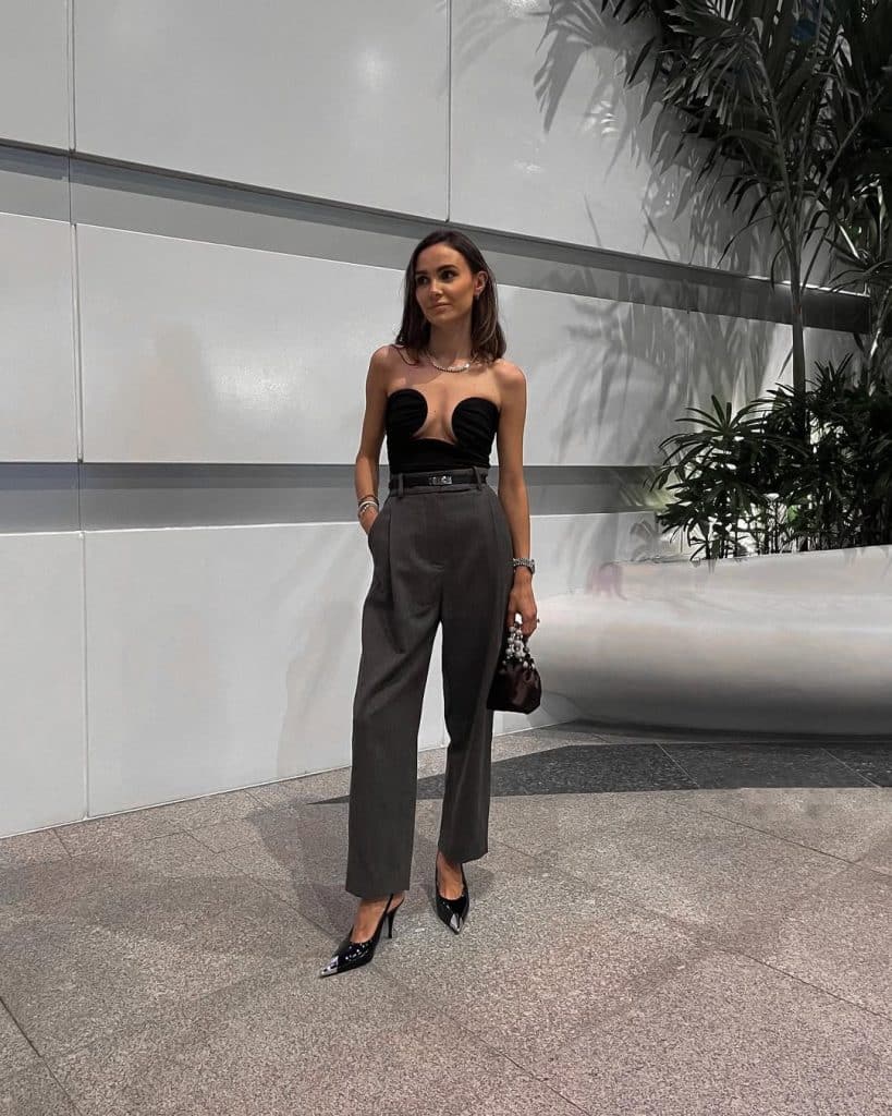 Woman wearing a black strapless top with high-waisted grey trousers and studded heels.