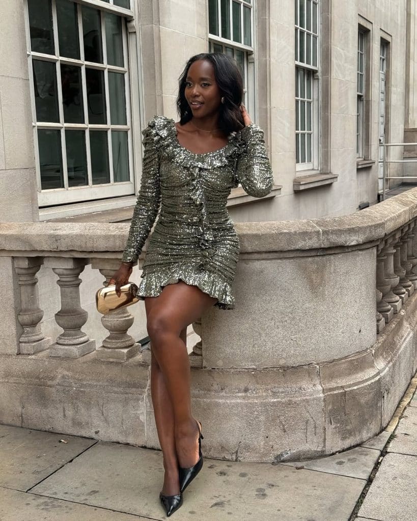 Woman in a silver sequin mini dress with puffed sleeves leaning against a stone balustrade.