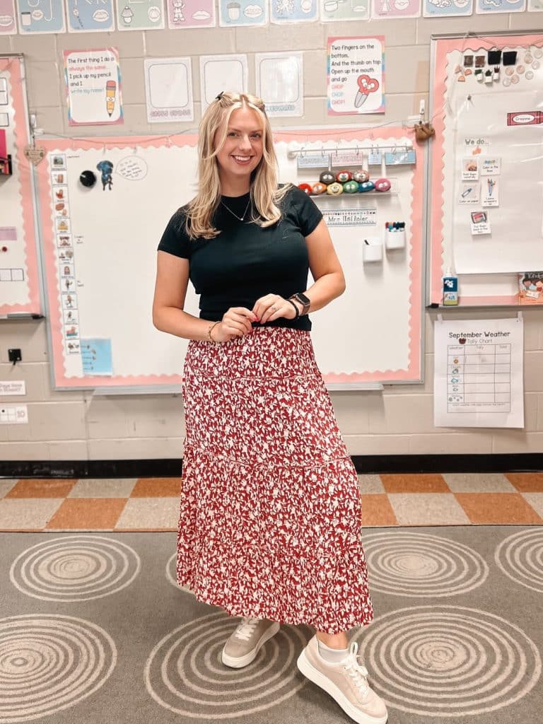 A woman in a red-and-white patterned tiered midi skirt standing in a classroom.