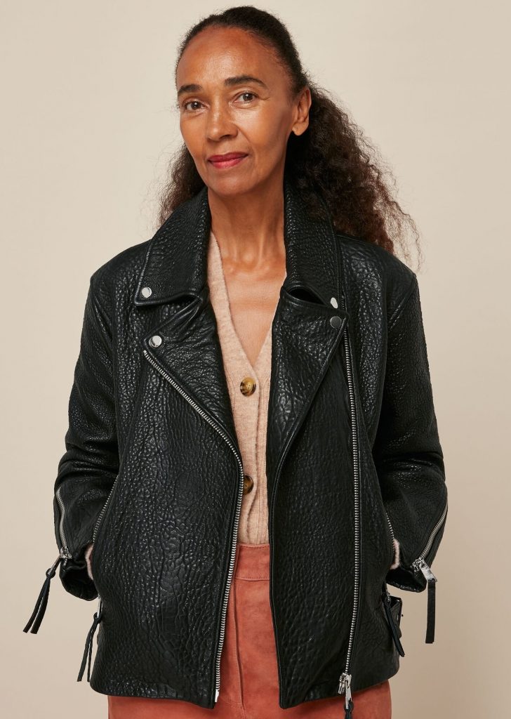 Black leather biker jacket worn with rust-colored trousers.
