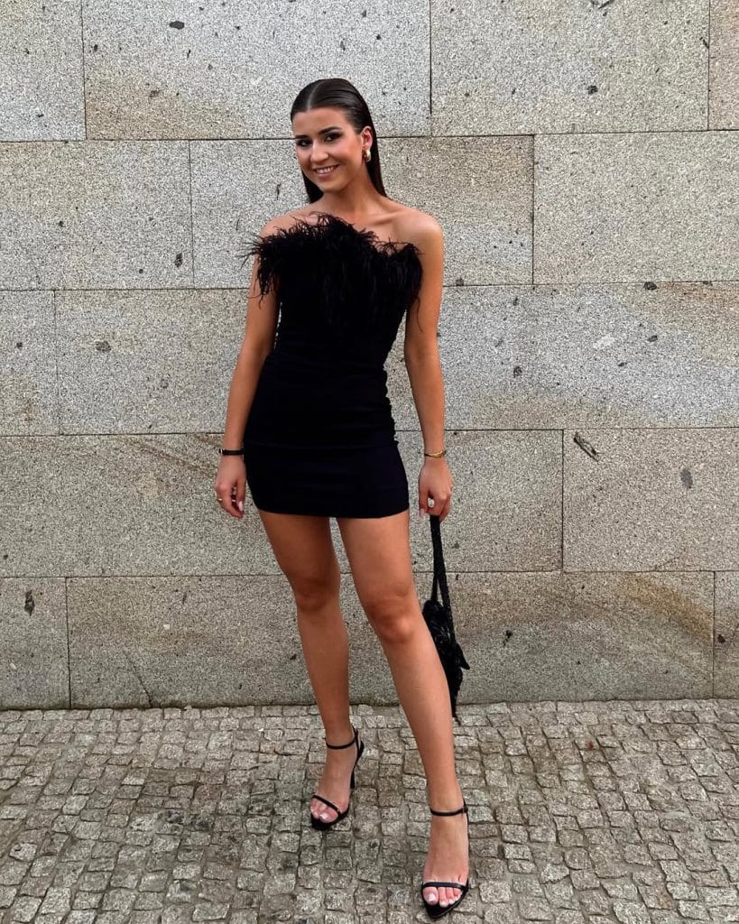 Woman in a black strapless feather-trimmed mini dress on a cobblestone street.
