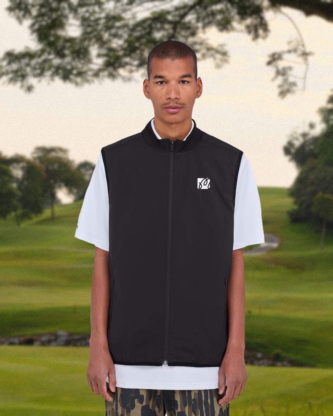 A model wearing a full streetwear-golf outfit walking through a city environment while carrying a contemporary golf bag.