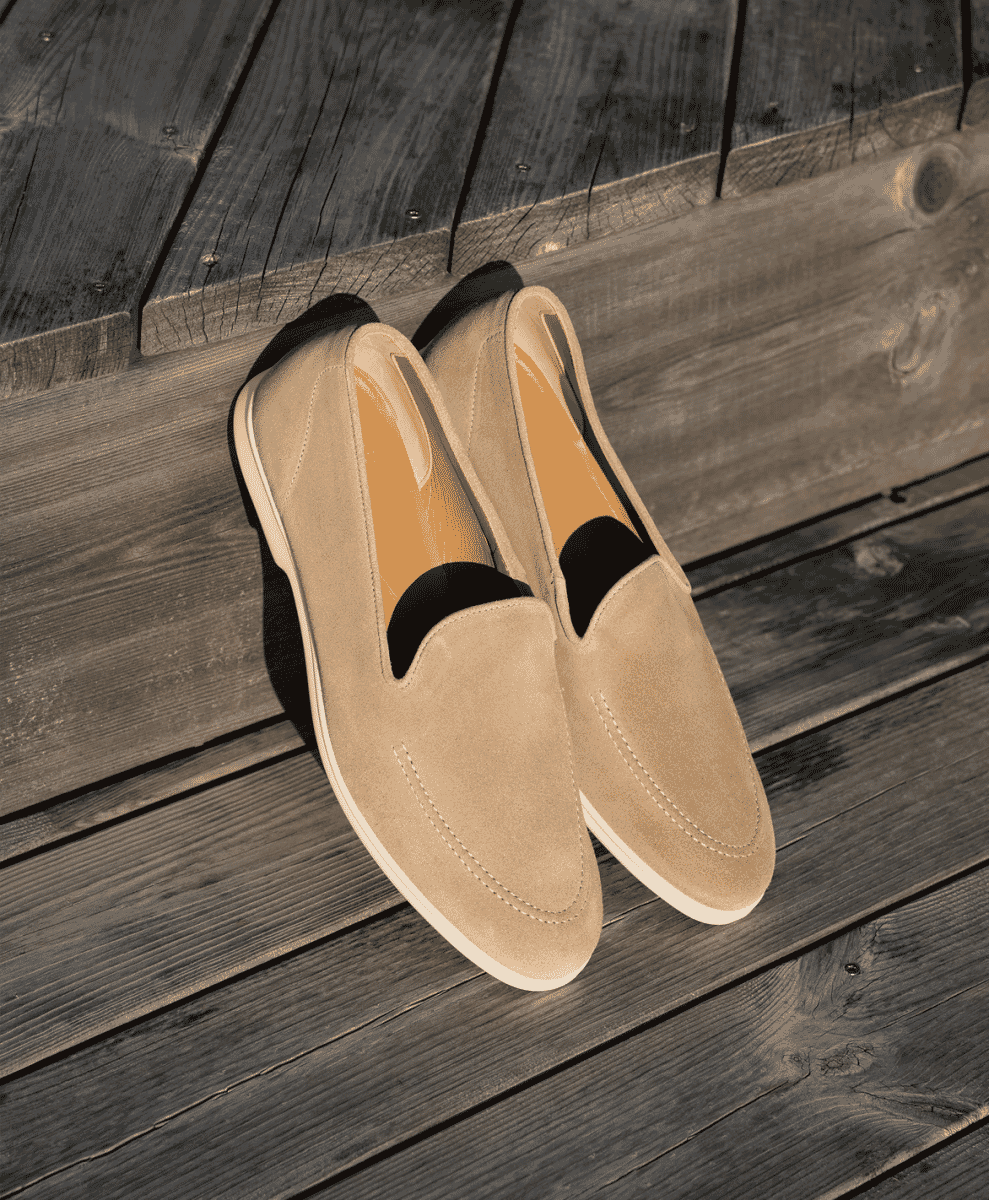 Beige suede loafers with white soles resting on a wooden deck.