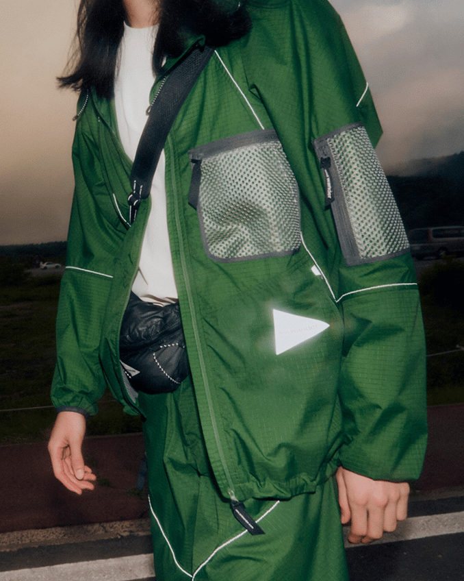 Green technical jacket with mesh pockets and reflective elements.
