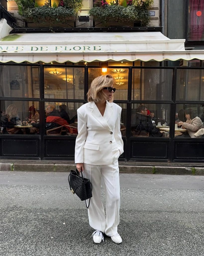 A woman in a white oversized blazer suit with flared trousers in front of a Parisian café.