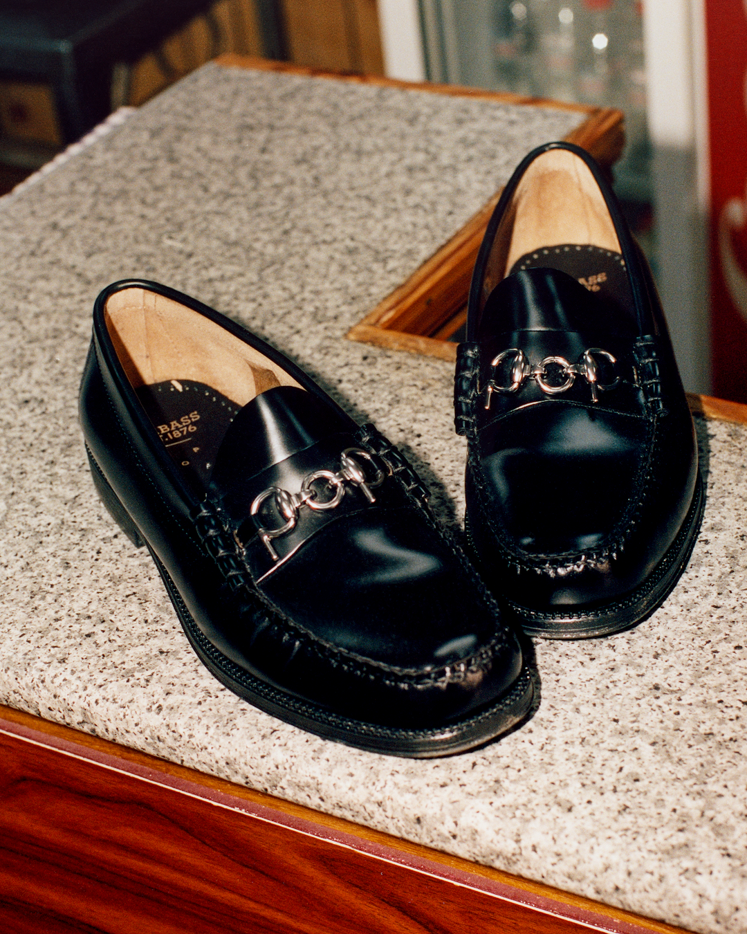 A pair of glossy black leather loafers with silver horsebit detailing on a speckled countertop.