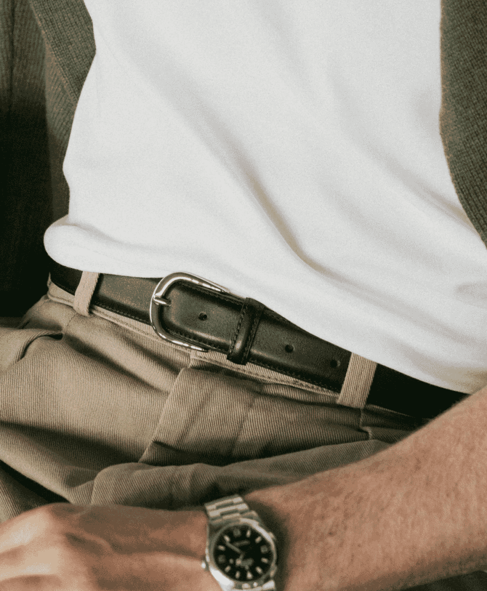 Close-up of a man's torso featuring a black leather belt, beige trousers, and a wristwatch.