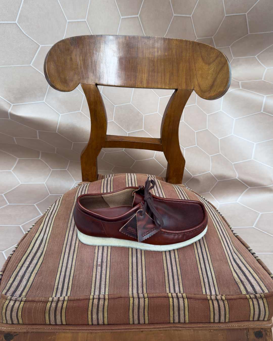 A brown leather desert boot on a striped wooden chair.