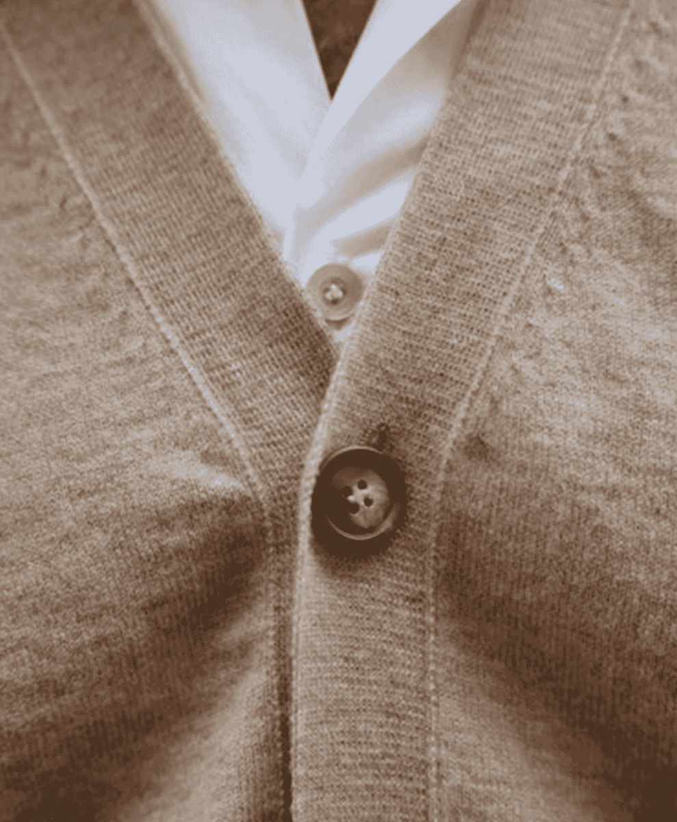 Close-up of a beige knitted cardigan with button closure over a white shirt.