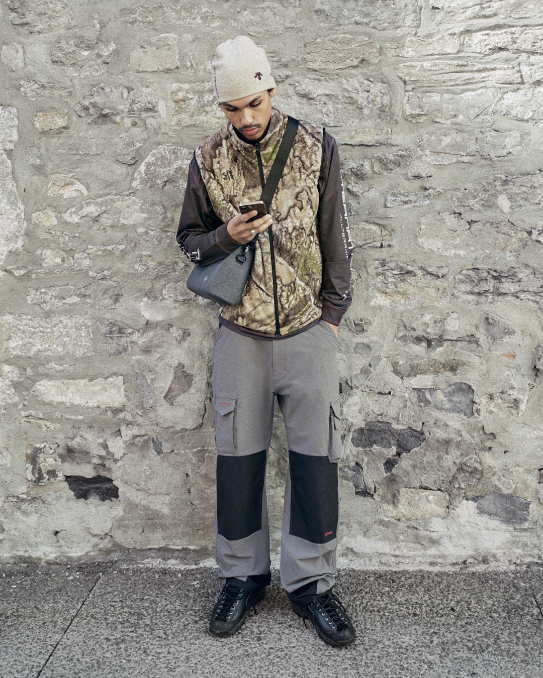 Man wearing a camouflage vest over a long-sleeve shirt with gray cargo pants.