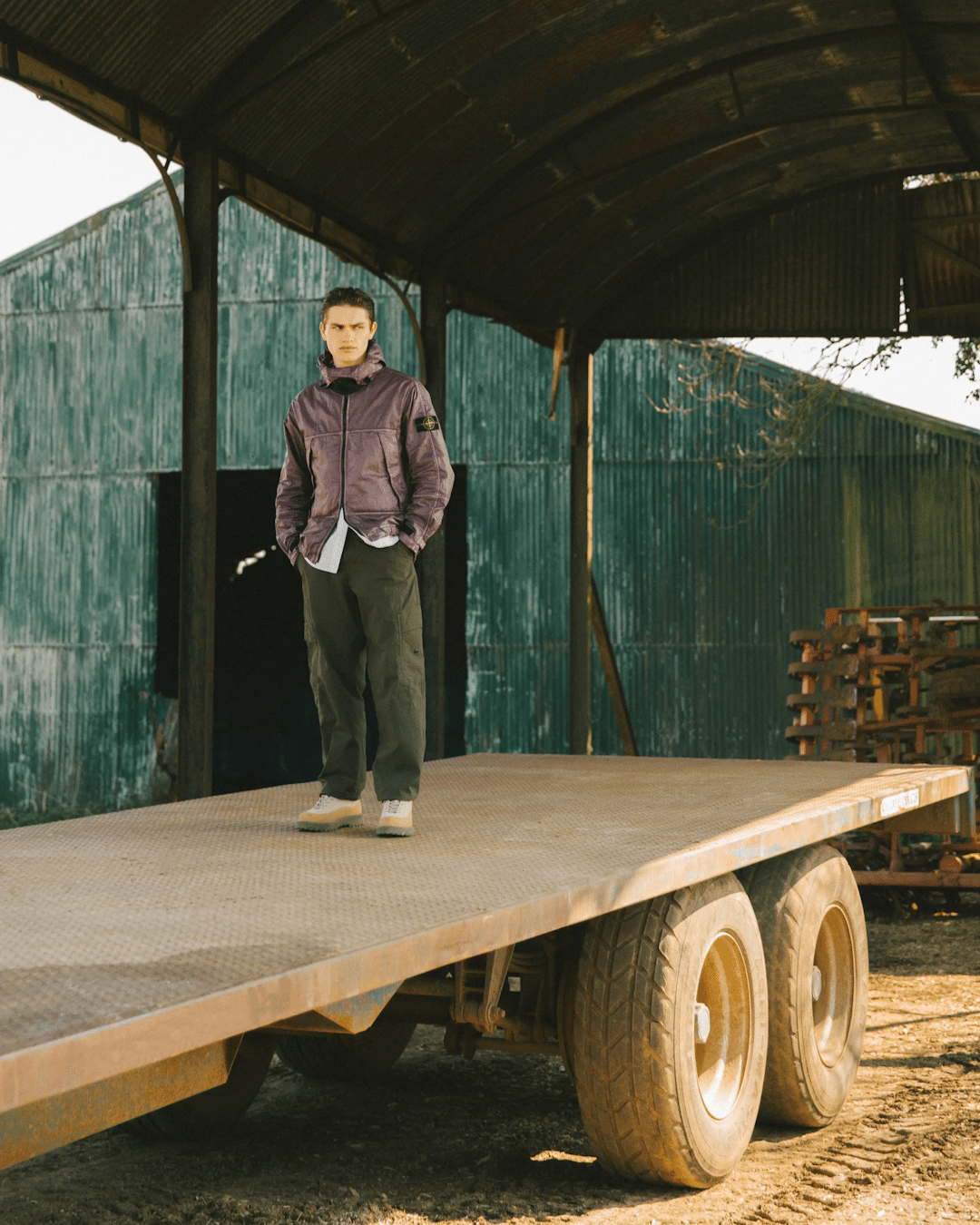 A man in a purple Stone Island jacket and cargo pants standing on a flatbed trailer.