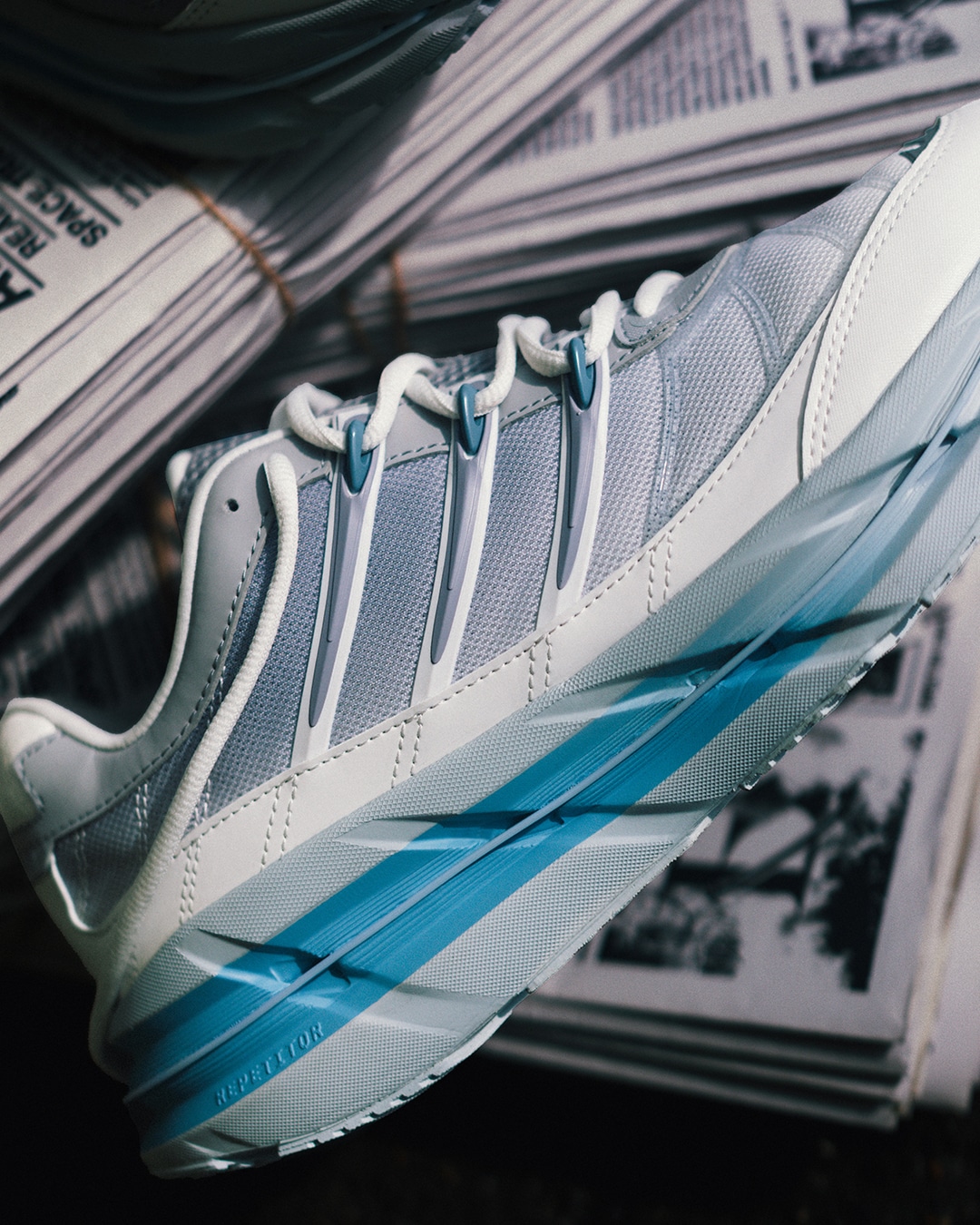 Close-up of the light gray and blue adidas HRMY sneaker resting on a stack of newspapers.