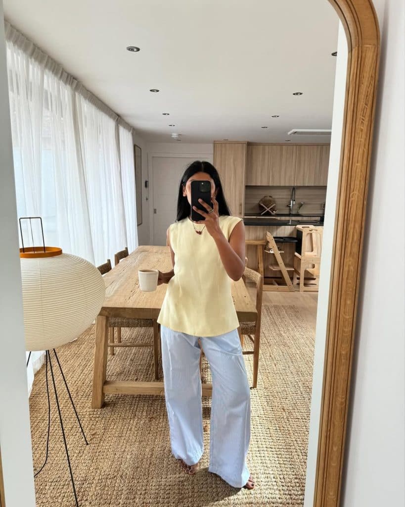 Mirror selfie of a woman wearing a yellow sleeveless top and white wide-leg pants.