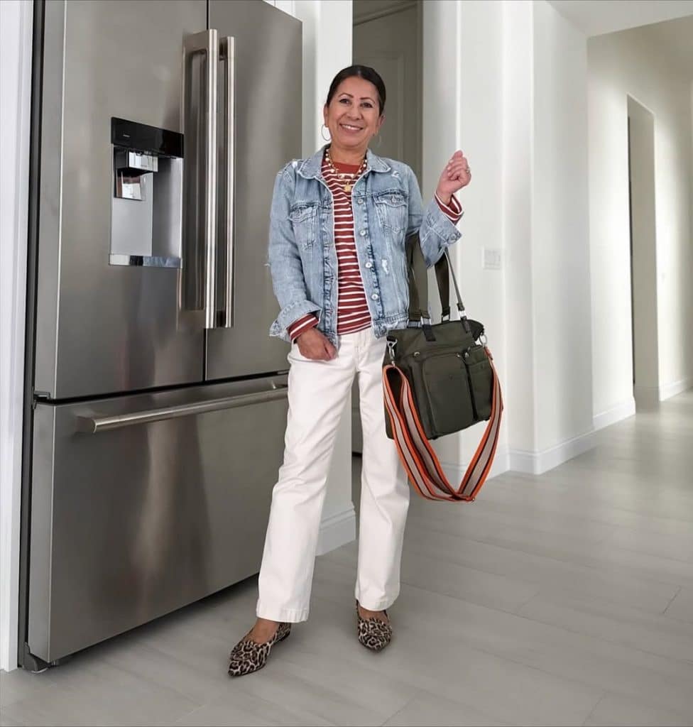 A woman in a denim jacket, striped top, and white wide-leg pants.