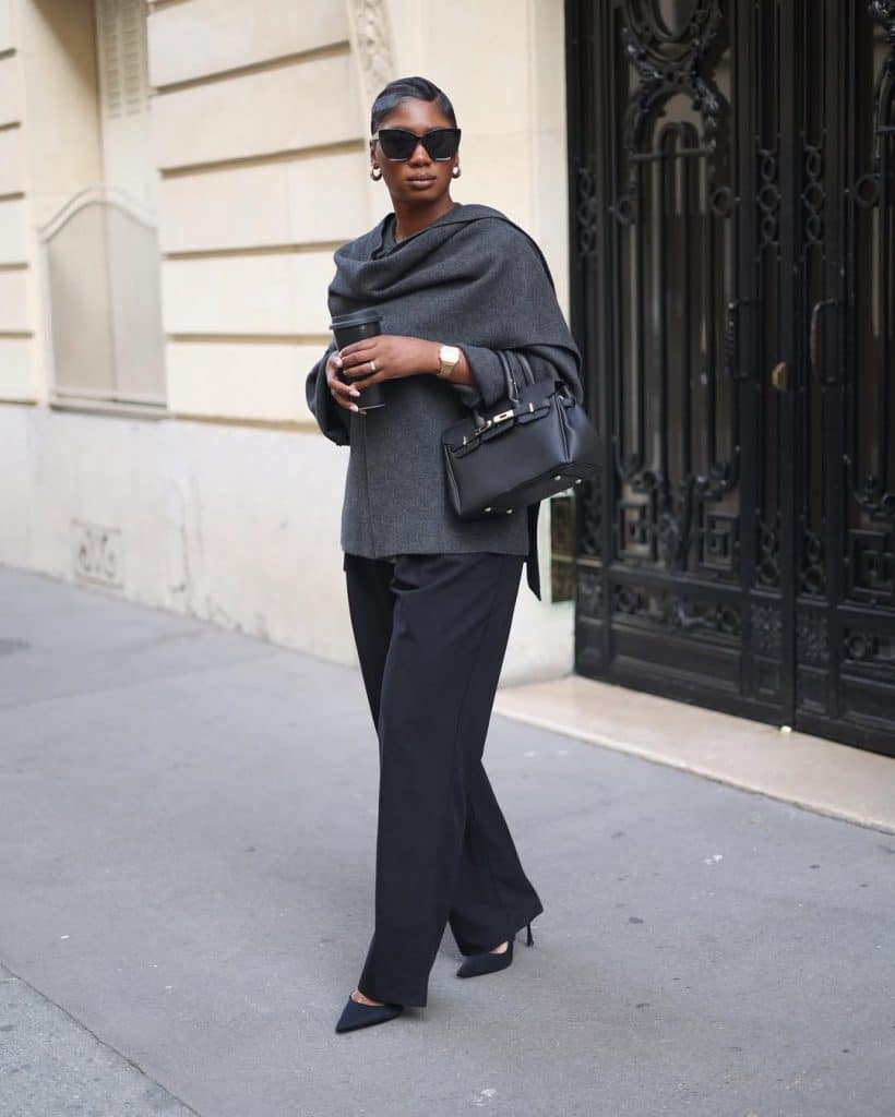 A woman walking in a gray draped top and black wide-leg trousers.