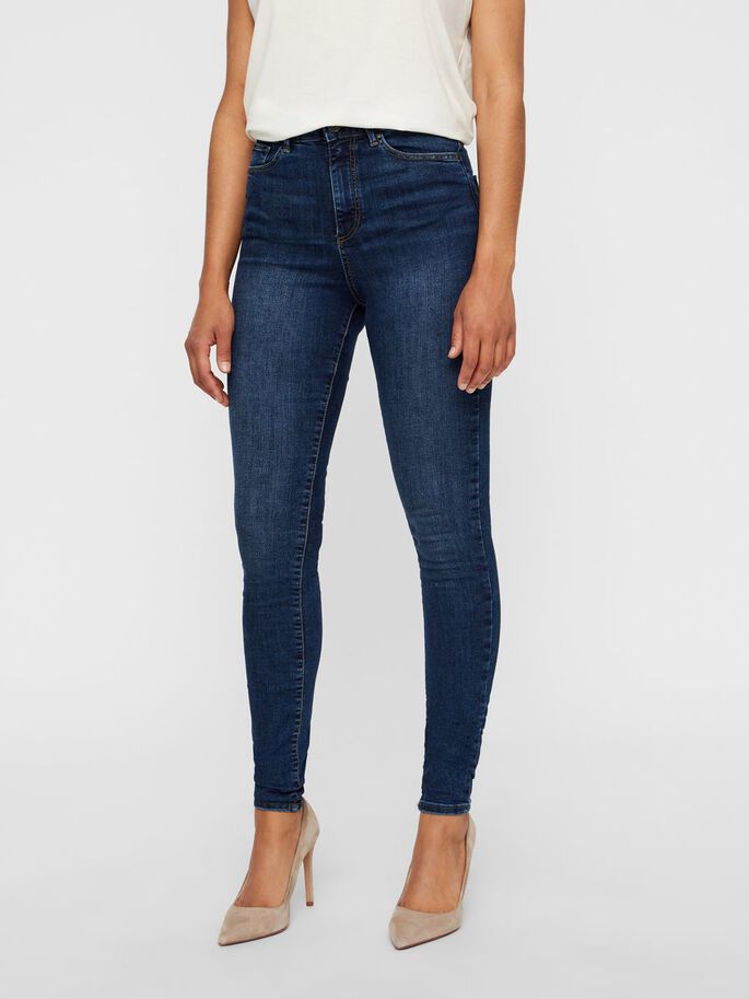 A woman modeling dark blue high-waisted skinny jeans and beige high heels.
