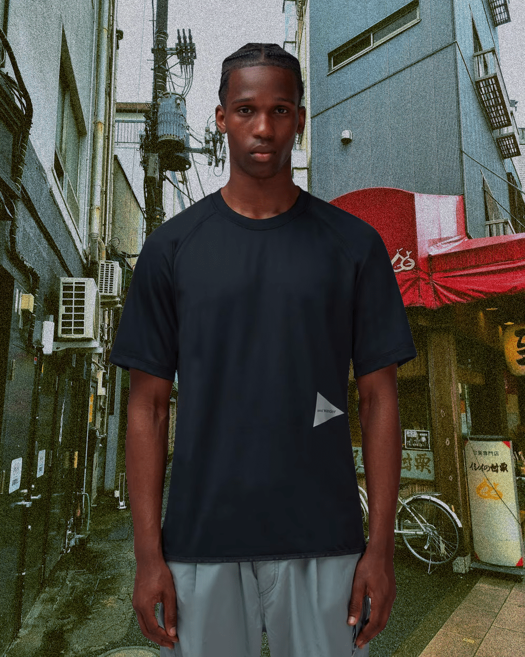 Man modeling a black technical T-shirt in a narrow Japanese alleyway.