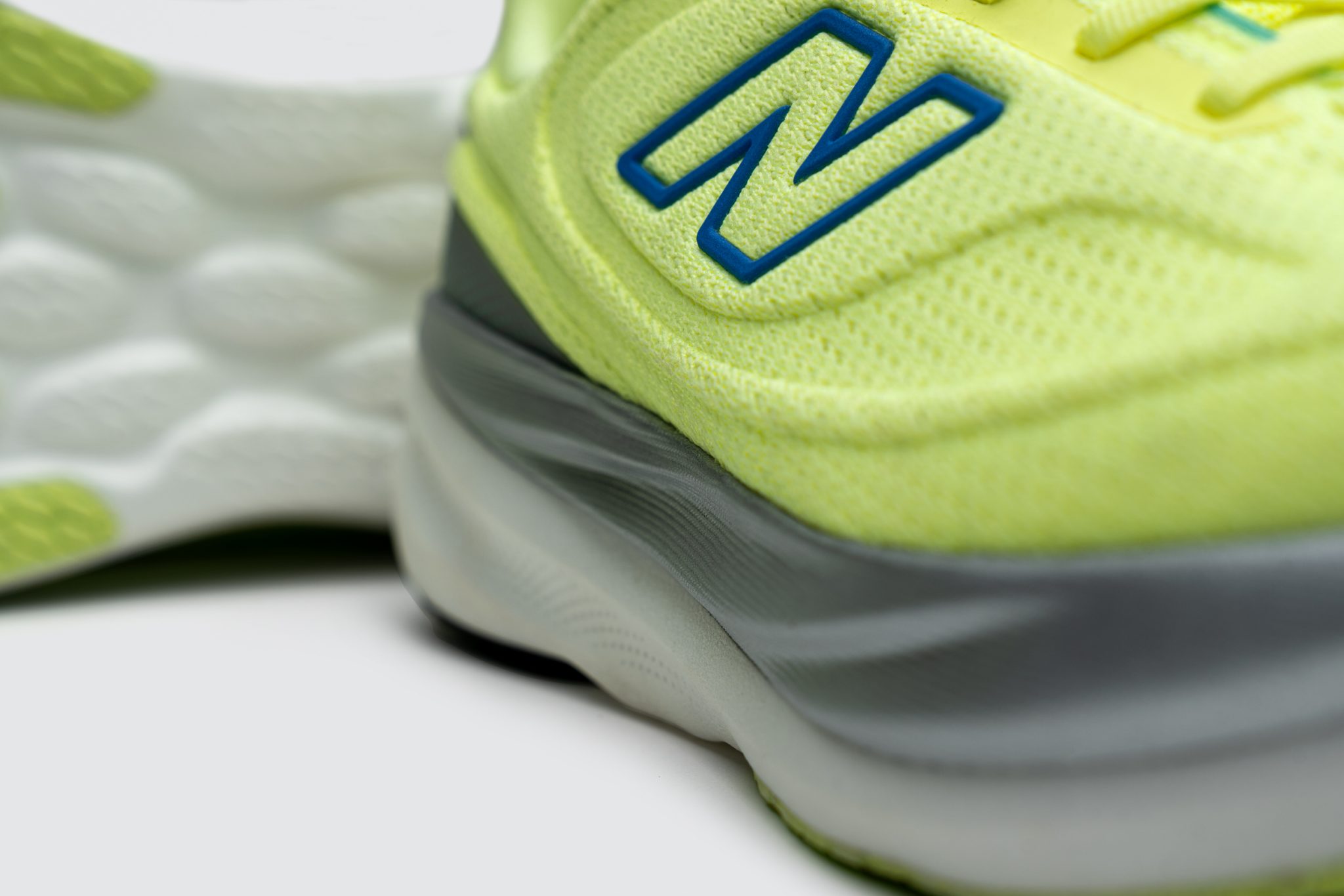 Detailed macro shot of the textured neon yellow mesh upper and layered midsole of the New Balance shoe.