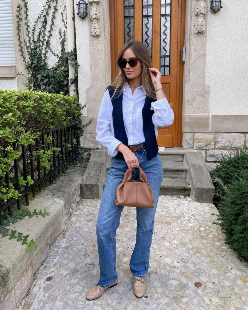 A woman in a navy vest and wide-leg blue jeans on a cobblestone path.