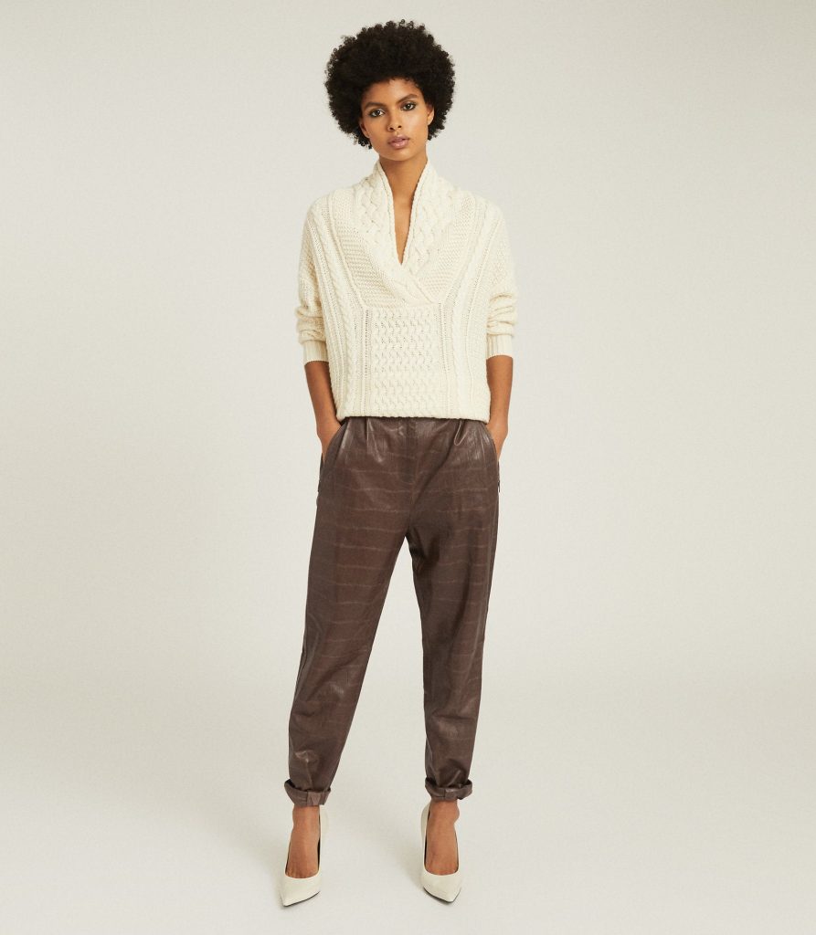 Cream cable-knit sweater paired with brown trousers.