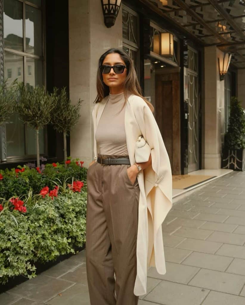 A woman in a long cream coat and wide-leg beige trousers on a city sidewalk.
