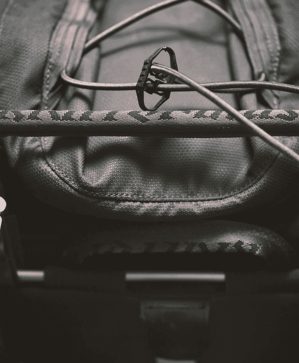 Black and white macro shot of a rugged backpack showing metal buckles and rugged fabric textures.