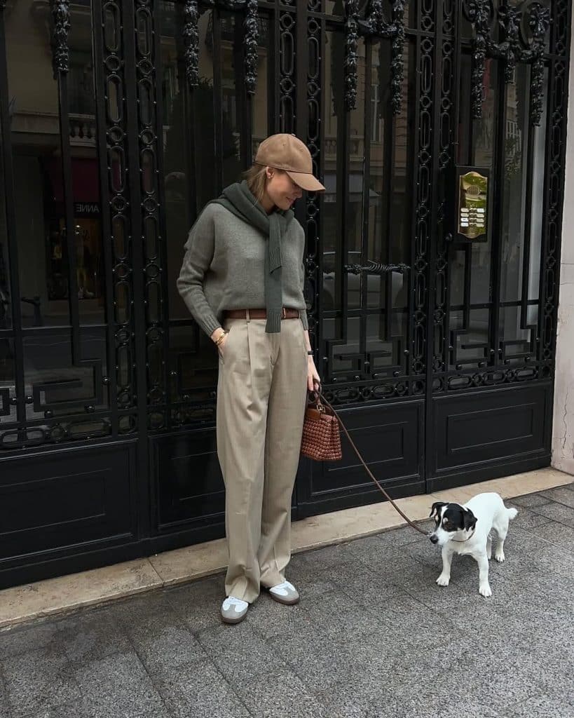 A woman in an olive green sweater, scarf, and wide-leg beige trousers.